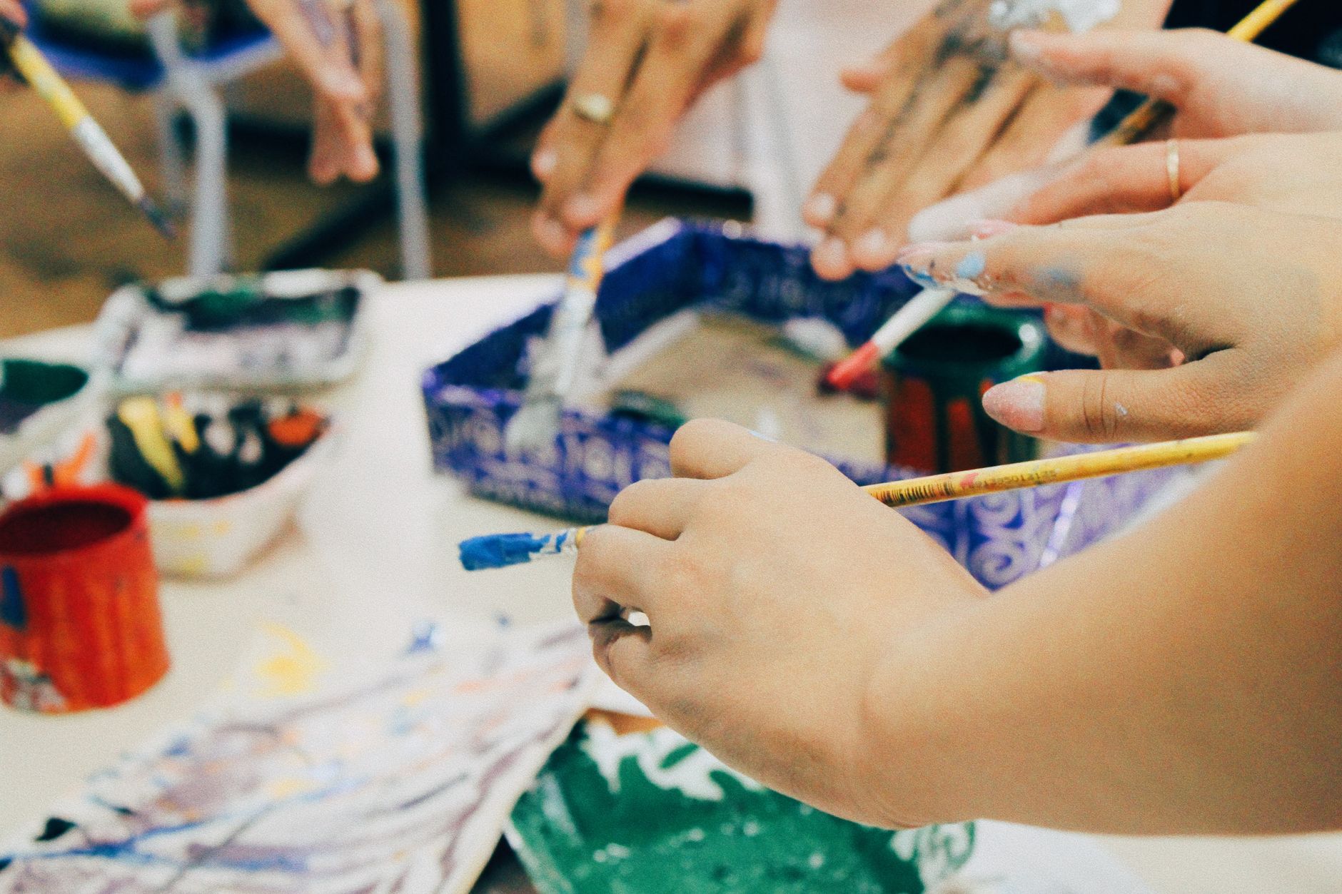 Children's hands painting together over trays of paint and paper
