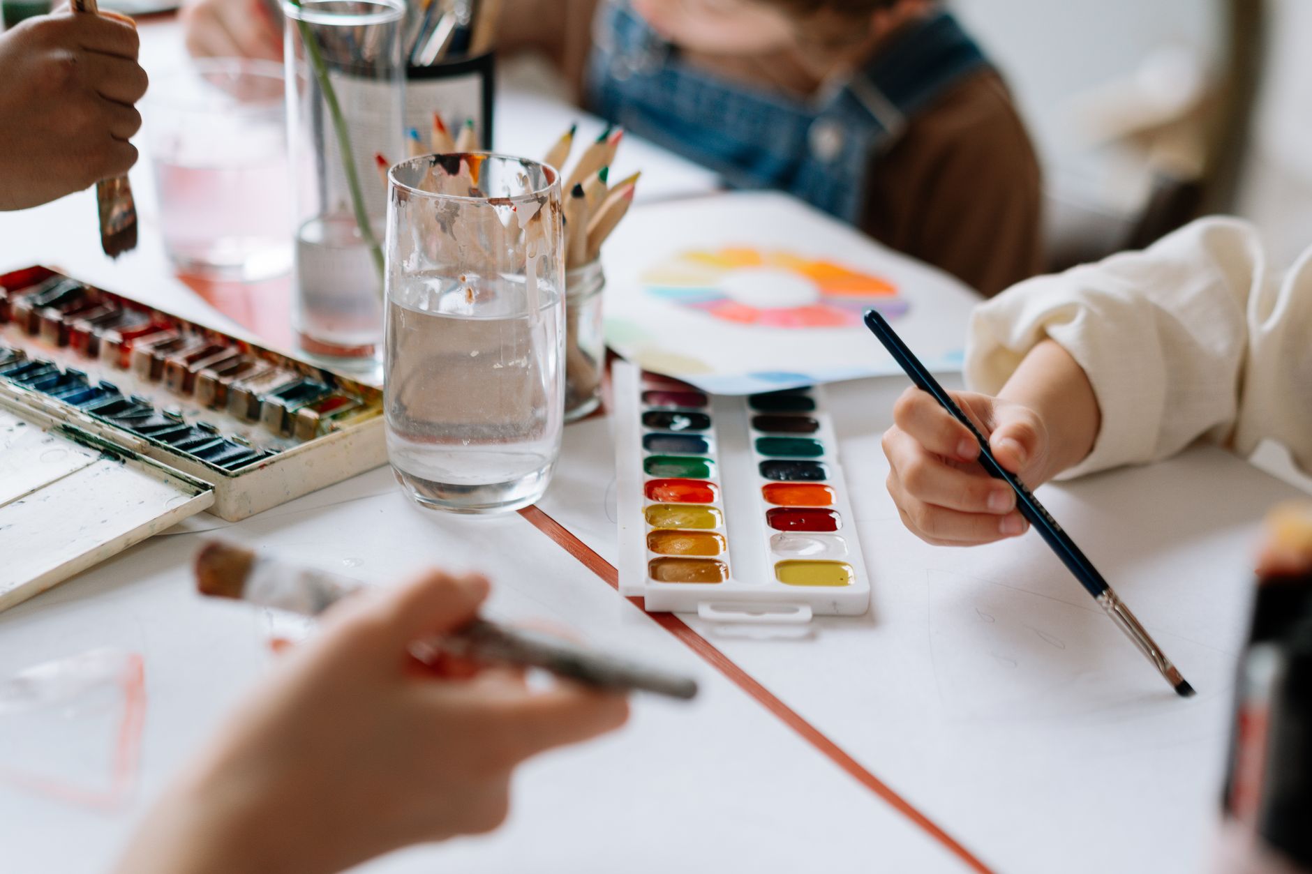 Watercolour palettes and brushes with children's hands mid-painting