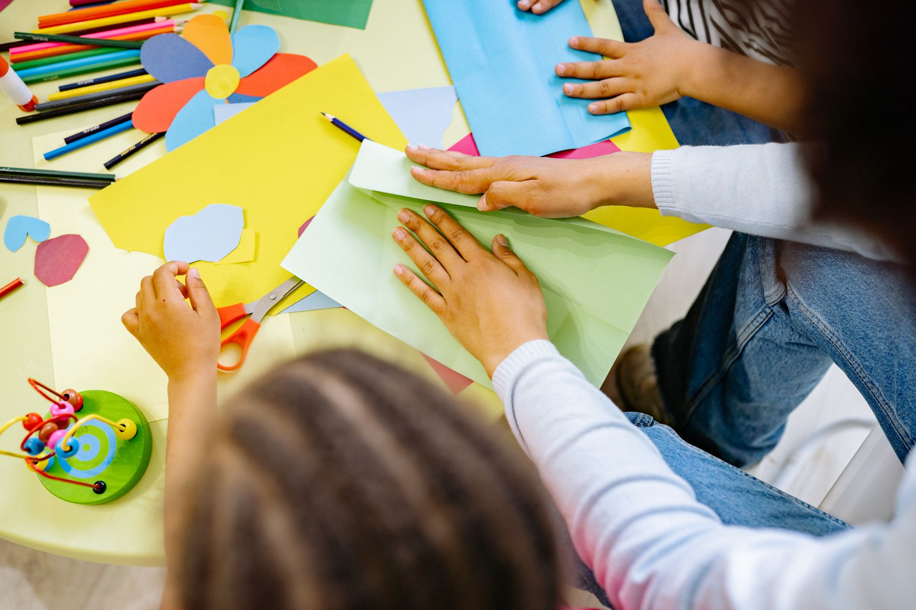 Children cutting and gluing bright paper shapes at a craft table