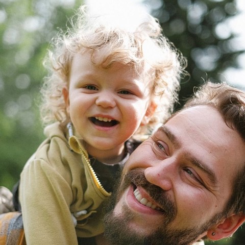 Tom, a Big Crayon parent, laughing with his curly-haired child on his shoulders