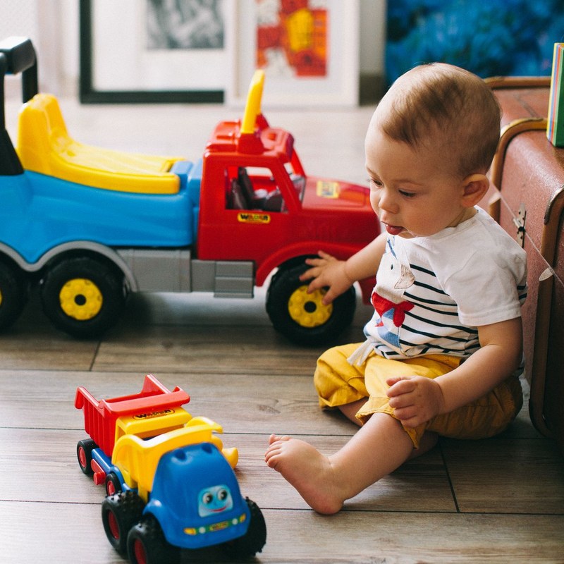 A baby sitting on a wooden floor playing with toy trucks