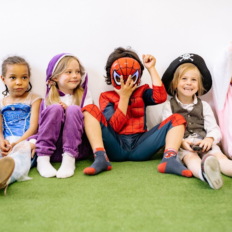 Five preschoolers in dress-up costumes sitting together on a green classroom floor