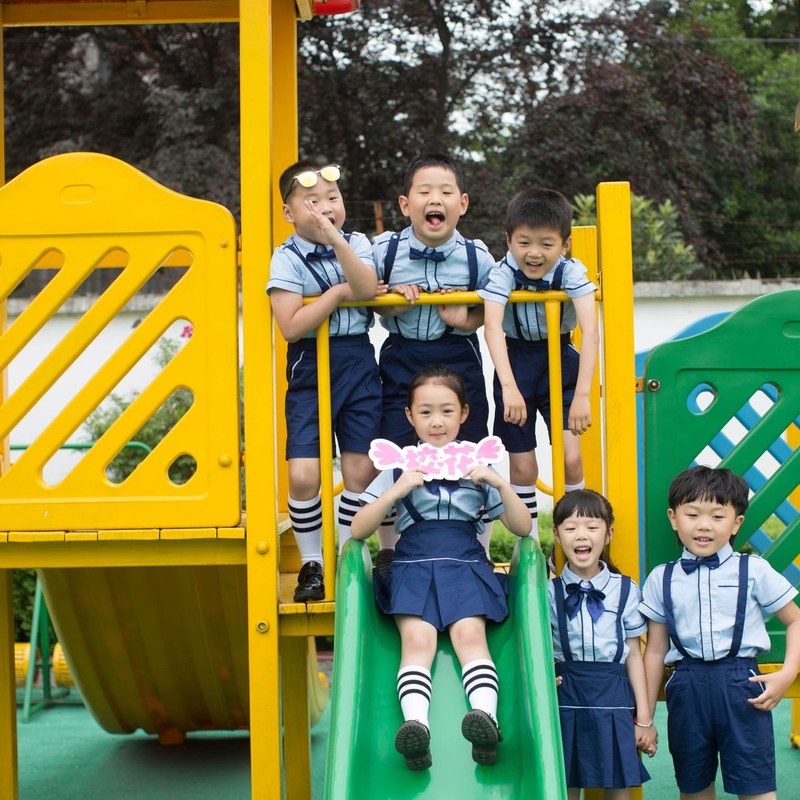 Kindergarten children in matching school uniforms playing on a yellow and green slide
