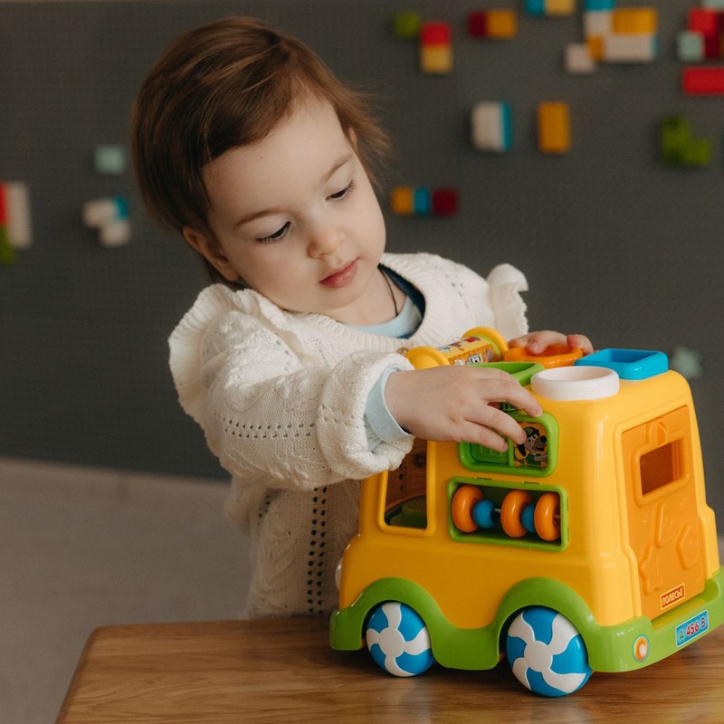 A toddler exploring a colourful toy bus with curious hands