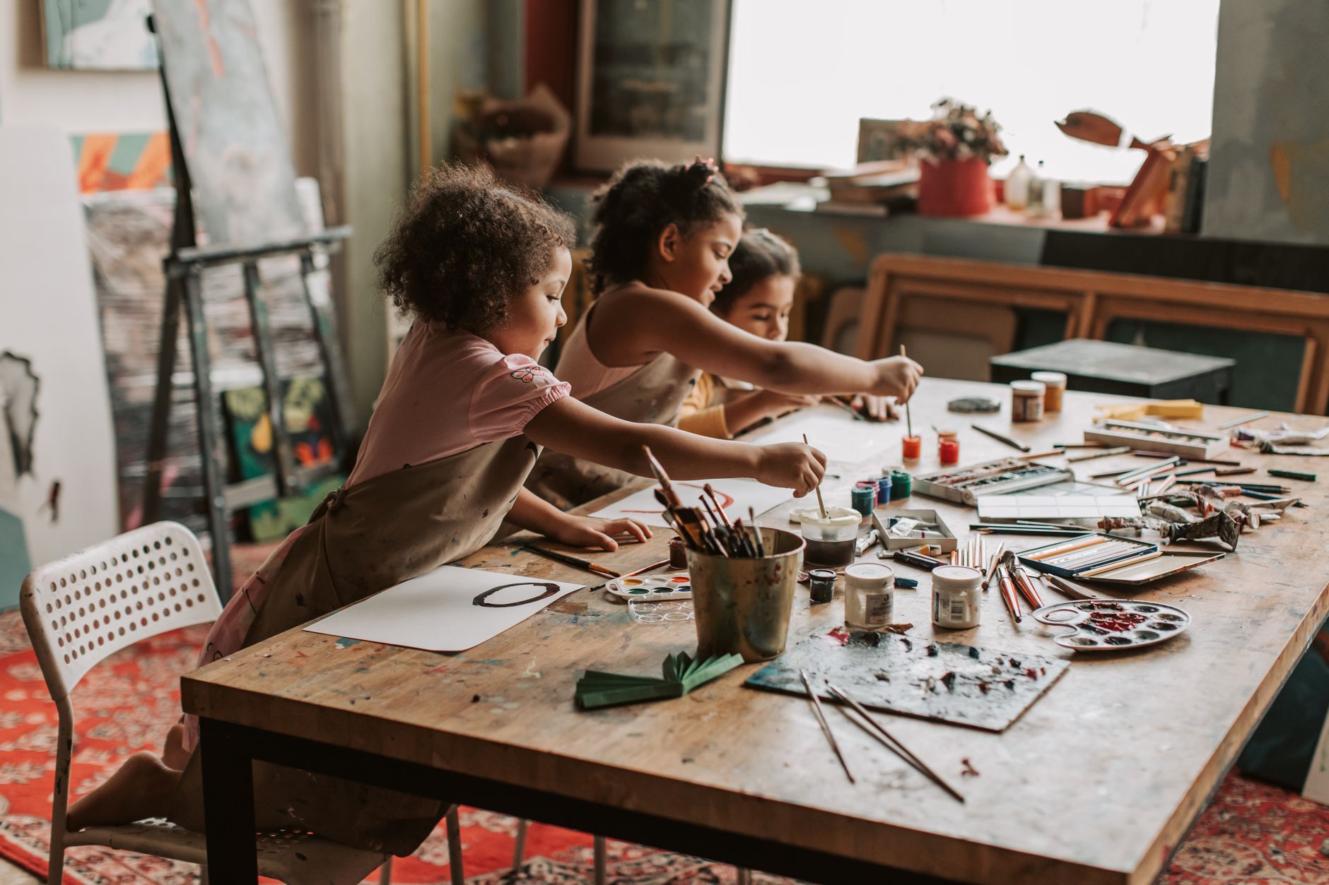 Children painting at a busy art table in a bright, studio-style classroom