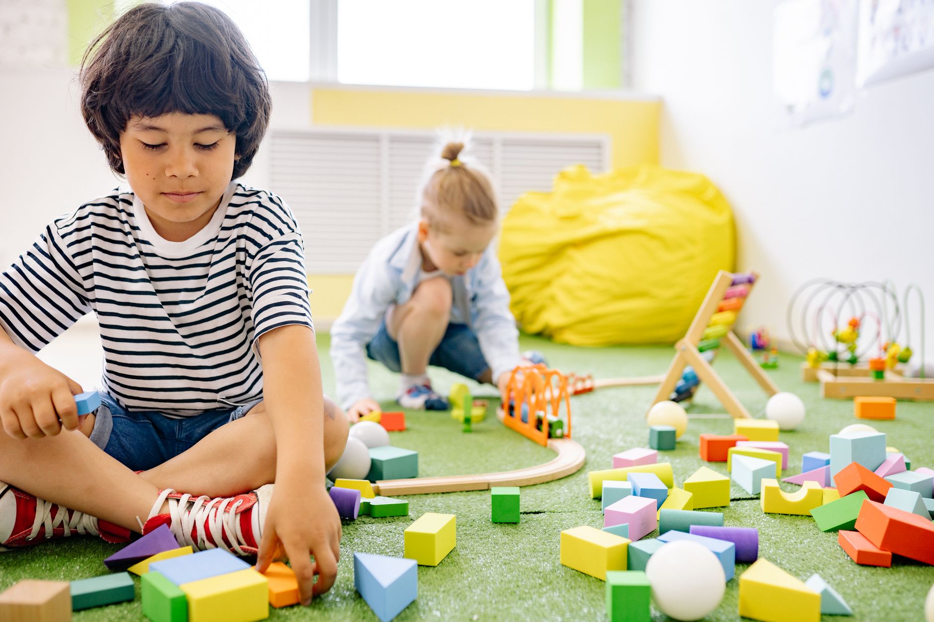 A boy in a striped shirt building with colourful wooden blocks on a play mat