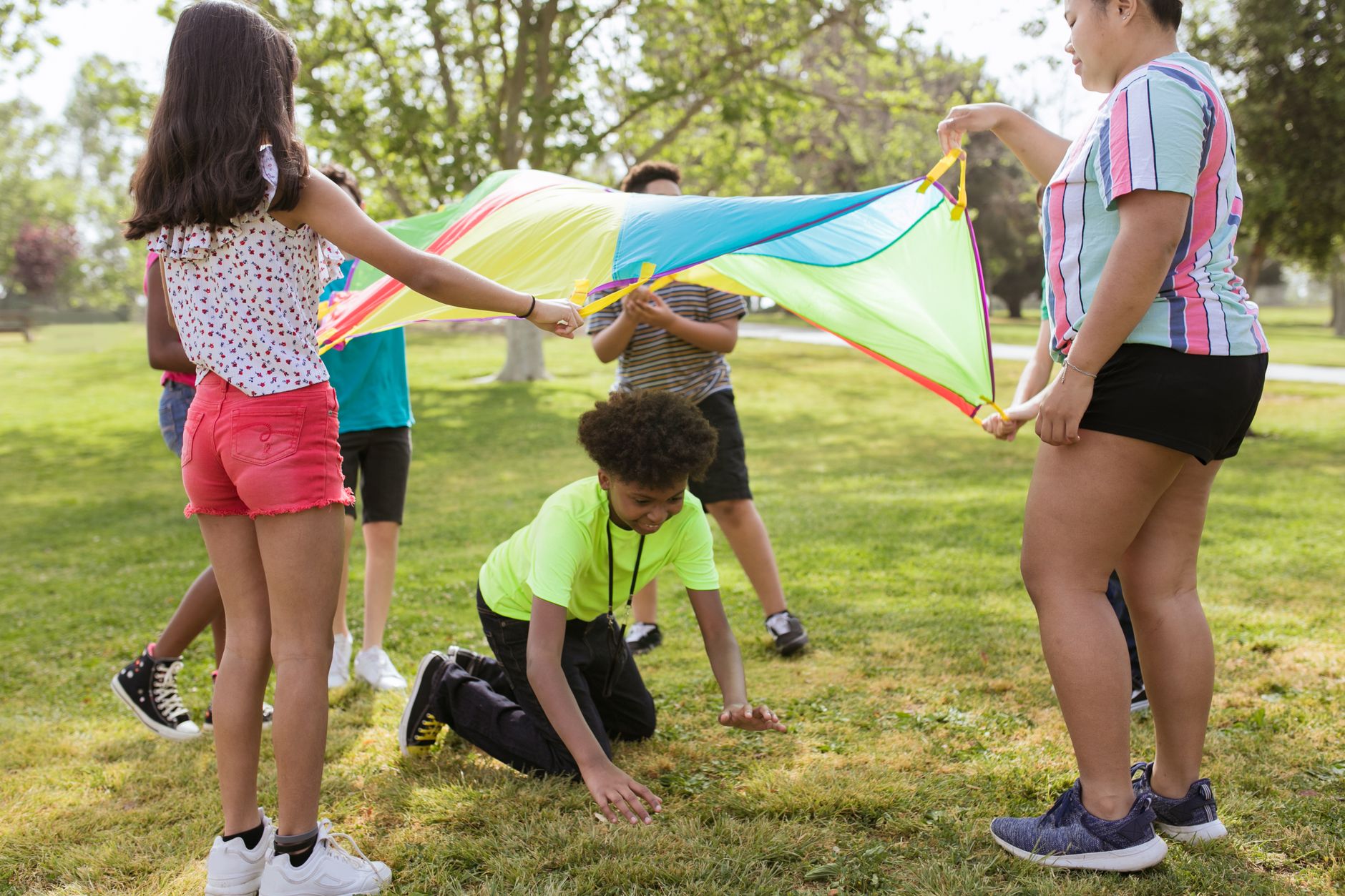 Children lifting a rainbow parachute together on a sunny grass field