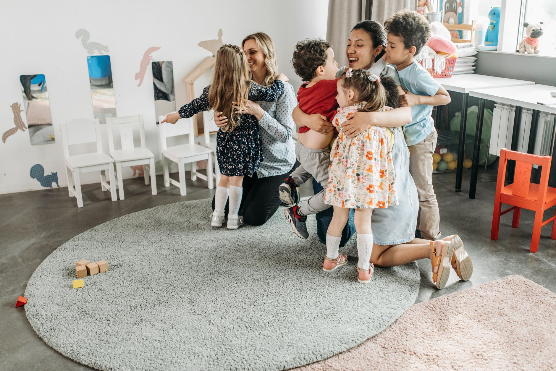 An educator hugging a group of young children on a soft rug